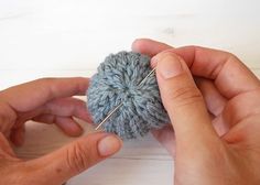 two hands working on a crocheted ball of yarn with pins in the middle