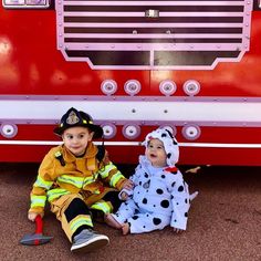 two children dressed in costumes sitting next to a fire truck