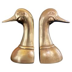 two brass ducks are standing next to each other on a white background, one is facing the opposite direction