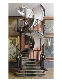 a spiral staircase in the middle of a room with paintings on the wall behind it