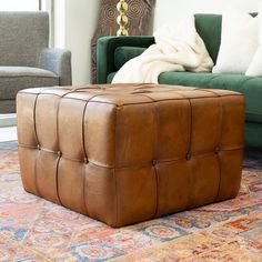 a brown leather ottoman sitting on top of a rug next to a green couch and chair