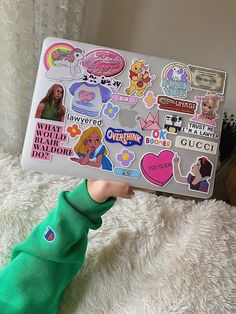 a person holding up a laptop with stickers on it