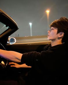 a man sitting in the driver's seat of a car with his hand on the steering wheel