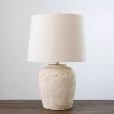 a white ceramic table lamp on a wooden table with a beige linen lampshade