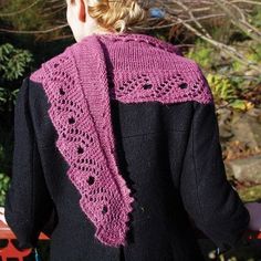 a woman wearing a pink knitted scarf on top of a wooden bench with trees in the background