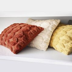 three decorative pillows sitting on top of a white shelf