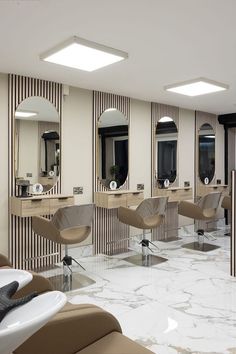 a salon with chairs, mirrors and lights on the walls in front of them is white marble flooring