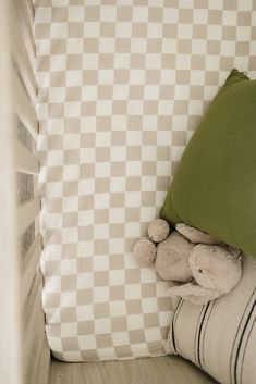 a teddy bear hiding under a pillow in a child's crib with checkered sheets