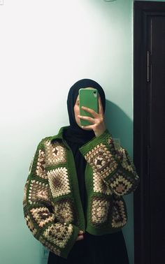 a woman taking a selfie in front of a mirror wearing a green and white crocheted jacket