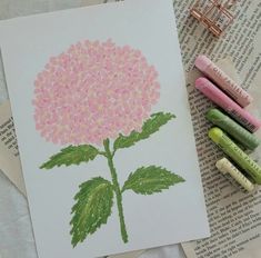 some crayons are laying next to a drawing of a pink hydrangea flower