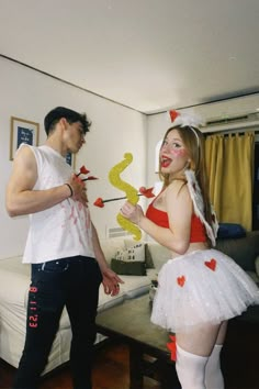 a man standing next to a woman in a living room wearing costumes and holding scissors