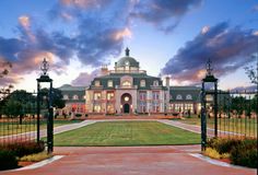 a large mansion with an iron gate leading into the front yard and driveway area at dusk