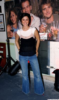 a woman standing in front of a movie poster holding a drink and smiling at the camera