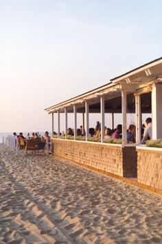 a group of people sitting on top of a sandy beach next to a restaurant covered in white awnings