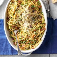 a white bowl filled with pasta and peas on top of a blue napkin next to silverware