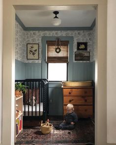 a baby sitting on the floor in front of a crib