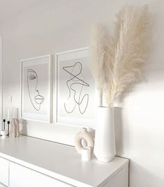 two white vases sitting on top of a white dresser next to paintings and candles