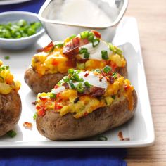 baked potatoes with bacon, cheese and green onions on a white plate next to peas