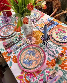 the table is set with colorful plates and flowers