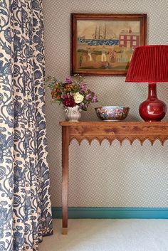 a red lamp sitting on top of a wooden table next to a vase filled with flowers