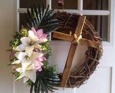 a wreath with flowers and a cross hanging on the front door to someone's house