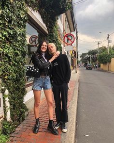 two people standing next to each other in front of a building with ivy growing on it