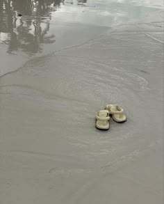 two pairs of shoes sitting in the sand at the edge of a body of water