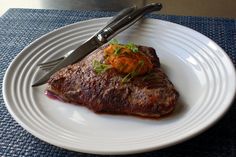 a piece of steak on a white plate with a knife and fork