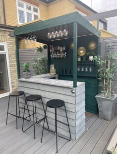 an outdoor bar with three stools on the deck next to plants and potted plants