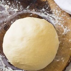 a ball of dough sitting on top of a wooden cutting board next to powdered sugar