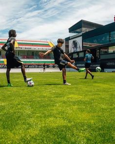 three young men kicking soccer balls on a field in front of an empty bleachers