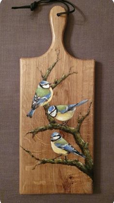 a wooden cutting board with birds painted on it and one bird perched on the tree branch