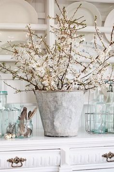 a vase with flowers in it sitting on top of a white dresser next to plates