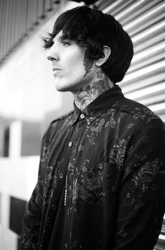 black and white photograph of a man with tattoos on his neck, standing in front of a building