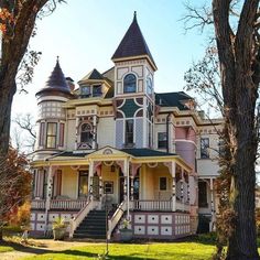 an old victorian style house in the middle of trees and grass with stairs leading up to it