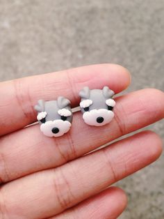 a person is holding two small earrings in their hand and they are both wearing grey and white