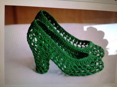 a pair of green crocheted high heels sitting on top of a white surface