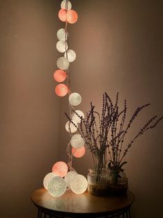 a table topped with a vase filled with flowers next to a string of light balls