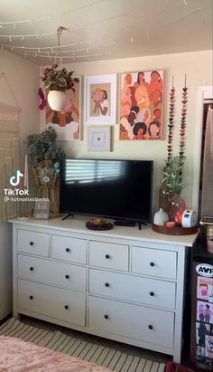 a flat screen tv sitting on top of a white dresser next to a wall filled with pictures