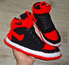 someone is holding up some crocheted shoes with red and black accents on them