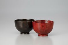 two wooden bowls sitting side by side on a white surface with one black and the other red