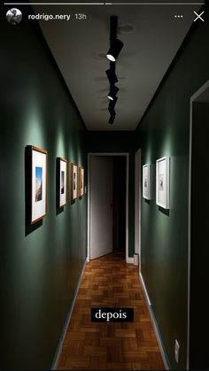 an empty hallway with green walls and pictures on the wall, along with a dark wood floor