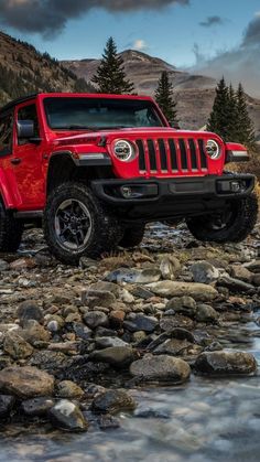 a red jeep parked on top of a rocky river