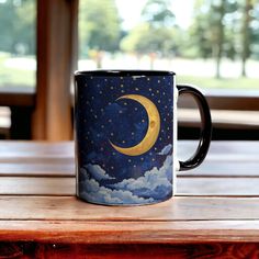 a coffee mug with the moon and stars painted on it sitting on a wooden table