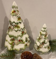 two ceramic christmas trees sitting on top of a table next to pine cones and decorations