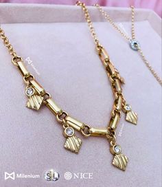 a gold necklace with charms on it sitting on top of a pink cushioned surface