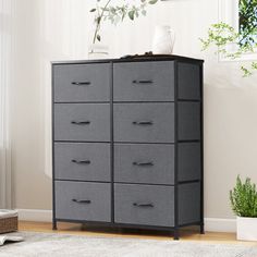 a gray dresser with drawers in a room next to a window and potted plant