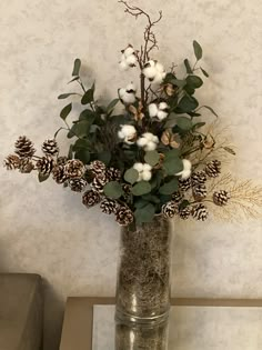 a vase filled with cotton and greenery on top of a table next to a wall