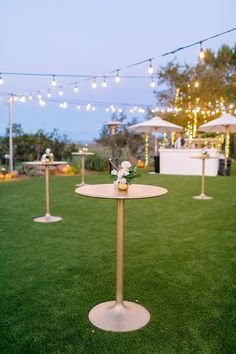 a table with flowers on it in the middle of some grass and lights strung overhead