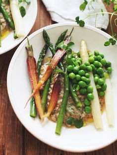 a white plate topped with asparagus, peas and carrots on top of a wooden table